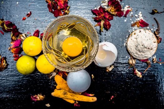 Face mask of lemon juice, honey, and curd along with some raw turmeric well mixed in a glass bowl along with entire raw ingredients on the wooden surface for acne-prone skin and blemishes.