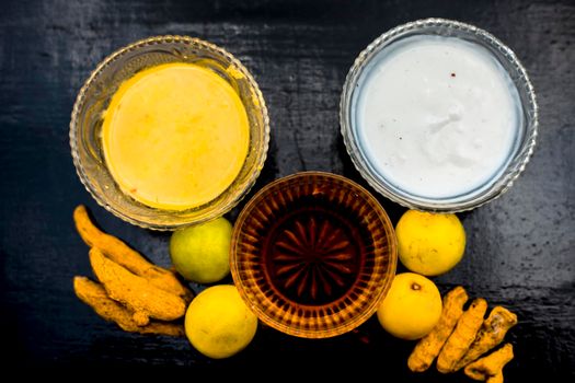 Face mask of lemon juice, honey, and curd along with some raw turmeric well mixed in a glass bowl along with entire raw ingredients on the wooden surface for acne-prone skin and blemishes.