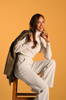 Portrait of tendy woman with trench coat on shoulder posing on beige background. Fashion studio photo, Autumn and Winter concept.