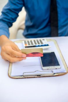 Close up of employee holding a smart cell phone and credit card in his hand wearing a blue colored shirt and black necktie. Concept of banking and shopping isolated on white.