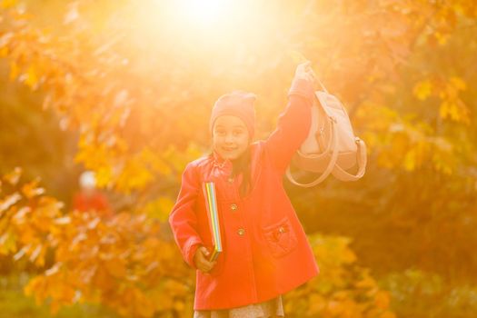Little cute girl runs along autumn park and kicks up fallen leaves. Schoolgirl with a backpack goes from school.The concept of autumn, school, study, education, childhood, back to school.