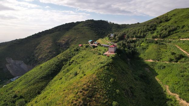 On a high green hill there are cottage houses. Green grasses and trees grow. Gray clouds in the sky. It is clear that the mudslide has descended in places. Dangerous location of houses. Kazakhstan