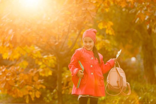 Little cute girl runs along autumn park and kicks up fallen leaves. Schoolgirl with a backpack goes from school.The concept of autumn, school, study, education, childhood, back to school.