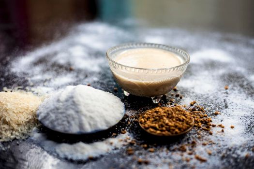 Hair growth remedy of rice flour water and fenugreek/coriander/parsley seeds powder on wooden surface and its paste in a glass bowl with some rice flour spread on the surface. Horizontal shot.