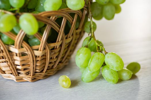 green autumn ripe grapes in a basket on a light wooden table
