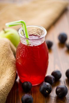 Sweet natural plum drink in a glass with a straw on a wooden table