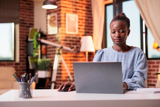 Successful businesswoman typing on laptop and working in modern home office. Smiling female freelance copywriter using portable computer in coprorate workspace with beautiful warm sunset light