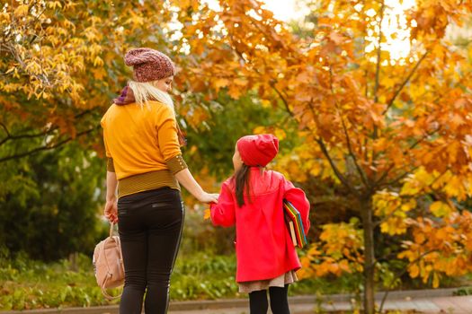 Mom leads her daughter to school. Return to school. Woman and girl with backpack behind the back. Beginning of lessons. First day of fall.