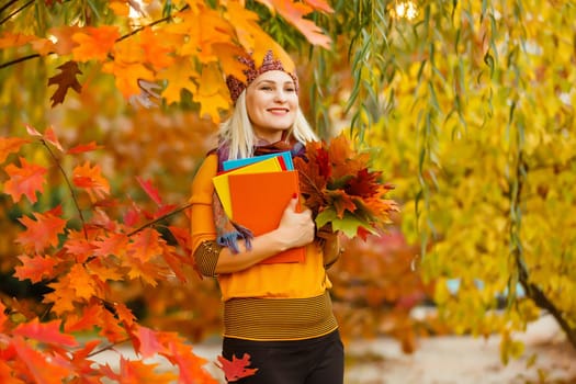 Young woman with autumn leaves in hand and fall yellow maple garden background