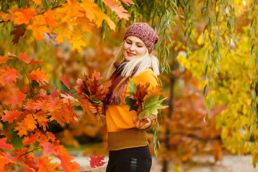 Young woman with autumn leaves in hand and fall yellow maple garden background