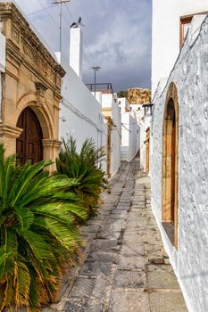 Narrow street in Lindos town on Rhodes island, Dodecanese, Greece. Beautiful scenic Lindos old ancient white houses with flowers. Famous tourist destination in South Europe. Lindos, Rhodes, Greece.