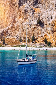Yacht anchoring in crystal clear turquoise water in front of the tropical island, alternative lifestyle, living on a boat. View of yacht at anchor on turquoise water, showing luxury, wealth.
