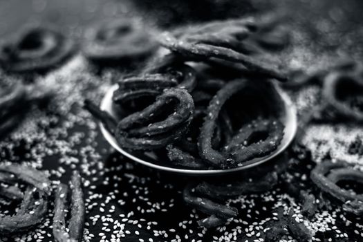 Famous Indian snack in a glass plate on the wooden surface along with raw sesame seeds or til spread on the surface.