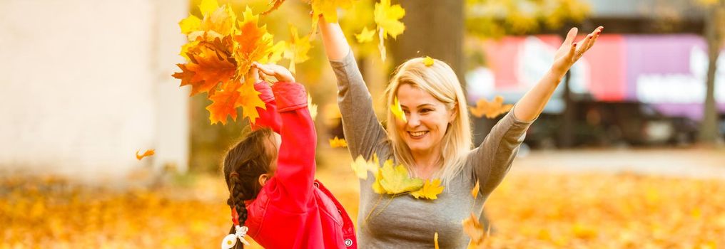 Happy parent and kid holding autumn yellow leaves outdoor.