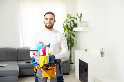 Young male worker of cleaning service with supplies on white background.