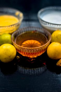 Face mask of lemon juice, honey, and curd along with some raw turmeric well mixed in a glass bowl along with entire raw ingredients on the wooden surface for acne-prone skin and blemishes.