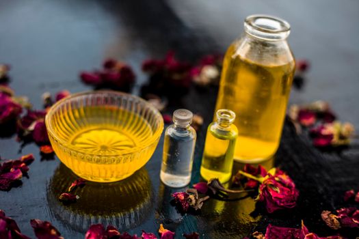 Close up of castor oil, tea tree oil, and some coconut oil in bottles on the wooden surface along with some raw honey and rose petals also present on the surface.