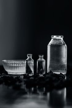 Close up of castor oil, tea tree oil, and some coconut oil in bottles on the wooden surface along with some raw honey and rose petals also present on the surface.