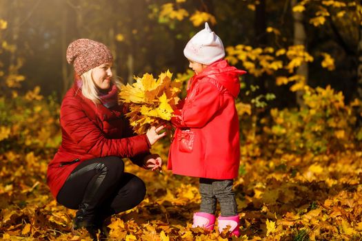 Mother drinking tea with kid daughter 4-5 year old sitting in sun light in park. Wearing autumn knitted clothes. Looking at each other. Motherhood. Childhood.