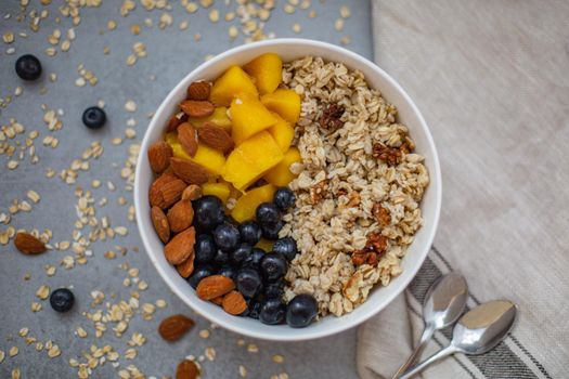 Oatmeal porridge with blueberries, mango and almonds in bowl on concrete grey table from above. flatlay. Healthy breakfast food. Copy space