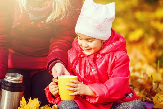 little girl drinks tea in the autumn park