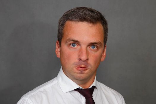 Man in white shirt on gray background makes a horrible grimace. Crazy guy. Negative emotion. Portrait of a man with a psychological illness.