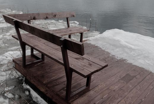 Wooden bench on the pier near the shore. Winter landscape with a bench near a winter lake.