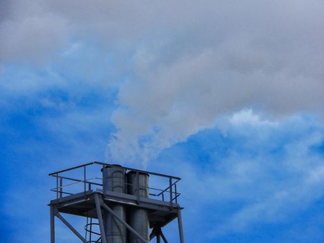 The chimney of the heating plant pollutes the environment with white smoke.Smoke from the chimney against the blue sky.