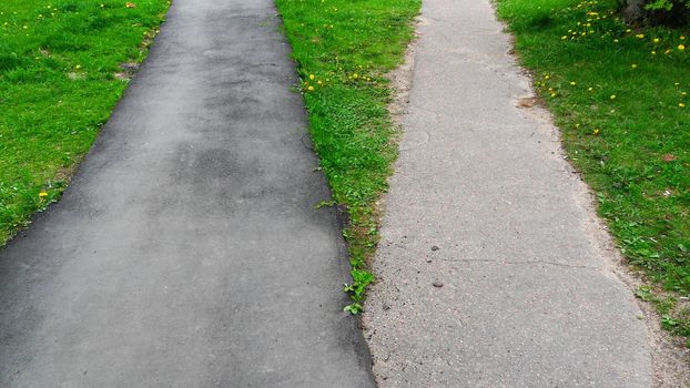 Two sidewalks from asphalt on green grass.