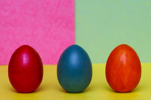 Two red and one blue handmade decorative eggs on a yellow, blue and purple background. Hand painted eggs on an abstract colorful background. Easter concept.