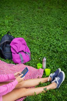 Top view of a young female student sitting on a plaid blanket and green grass in the park. Break in the open air, drink coffee, tea, sit on the phone