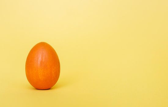 A wooden egg painted with orange paint against a light orange plaster background. Happy Easter background. Minimal Easter.