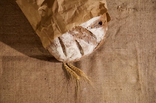 Artisanal bakery. Homemade sourdough bread and ears of wheat on table covered with linen tablecloth. Craft authentic wholesome whole grain rye bread. Home cooking. Food preparation. Selective focus