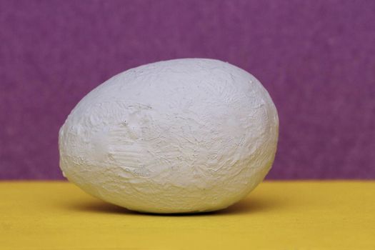 egg on two tone background. Easter ideas. A light blue hand painted decorative egg on a yellow and purple background.