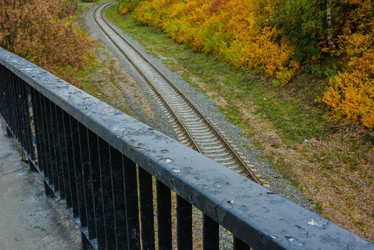 Railing of the old bridge on the background of the railway. The railway near the autumn forest. View of the railway from the old bridge. High quality photo