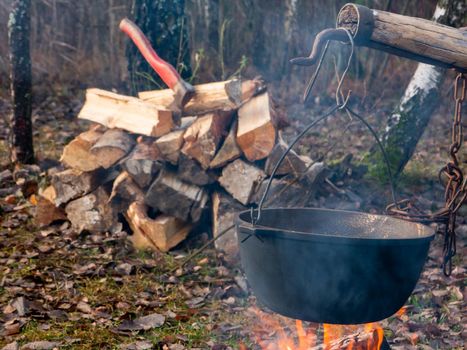 Picnic in the woods on an open fire. Pilaf cooking on fire outdoor. Hiking pot, Bowler in the bonfire. soup boils in cauldron at the stake.