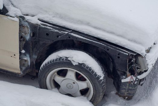 Old smashed car covered in snow.Fragment of an abandoned old car in the snow.