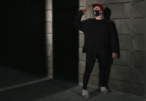 A man in a black sports uniform in a mask stands against the background of a wall illuminated by contrasting light.