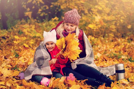 Mother and child hands in the autumn park in the middle of the orange fallen leaves