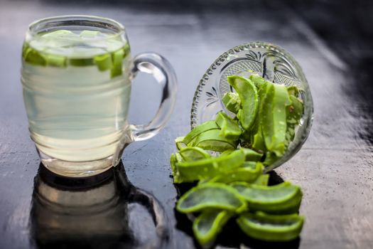 Close up of glass mug on wooden surface containing aloe vera detox drink in along with its entire raw ingredients with it. Horizontal shot with blurred background.