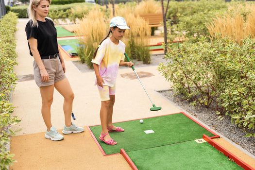 Mother playing with her cute daughter mini golf at outdoor playground