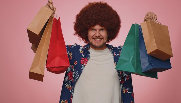 Happy tourist man with lush hair showing shopping bags, advertising discounts, smiling looking amazed with low prices, shopping on Black Friday holidays. Young bearded guy boy on blue background