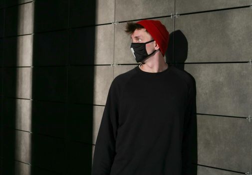 Portrait of a young man standing in a black t-shirt and black medical mask and red cap to protect against virus, covid-19 outbreak.