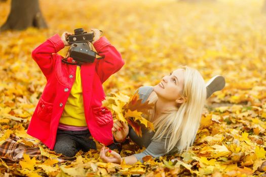 little girl plays with a camera in yellow leaves of autumn landscape