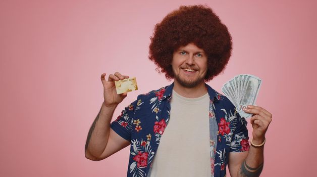 Happy tourist man showing plastic credit bank card advertising transferring money cashless, purchases online shopping, sale discount, internet order delivery purchase. Young guy boy on pink background
