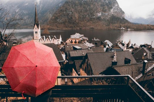 Girl holding a red umbrella looking at Hallstatt tourist town in Austria in a rainy day
