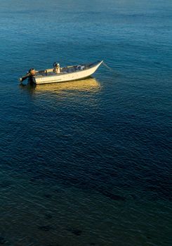 An old motor boat is anchored in the bay at sunset