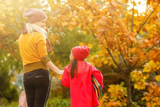 Mom leads her daughter to school. Return to school. Woman and girl with backpack behind the back. Beginning of lessons. First day of fall.