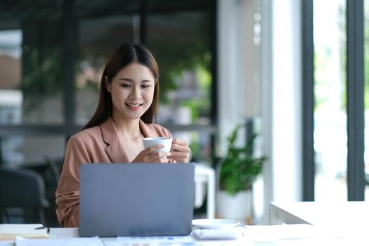 Smiling young Asian businesswoman holding a coffee mug and laptop at the office