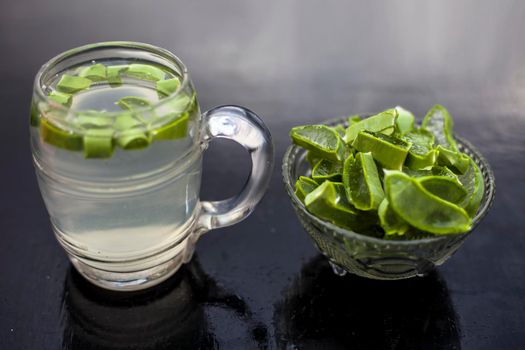 Close up of glass mug on wooden surface containing aloe vera detox drink in along with its entire raw ingredients with it. Horizontal shot with blurred background.